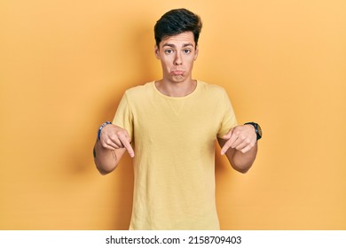 Young Hispanic Man Wearing Casual Yellow T Shirt Pointing Down Looking Sad And Upset, Indicating Direction With Fingers, Unhappy And Depressed. 