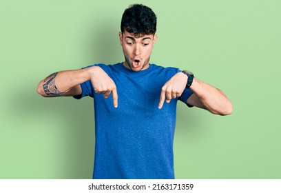 Young Hispanic Man Wearing Casual T Shirt Pointing Down With Fingers Showing Advertisement, Surprised Face And Open Mouth 