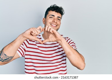 Young Hispanic Man Wearing Casual Clothes Smiling In Love Doing Heart Symbol Shape With Hands. Romantic Concept. 