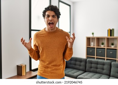 Young hispanic man wearing casual clothes standing at home crazy and mad shouting and yelling with aggressive expression and arms raised. frustration concept.  - Shutterstock ID 2192046745
