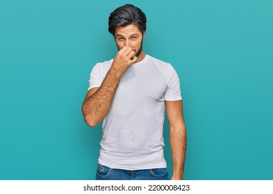 Young hispanic man wearing casual white t shirt smelling something stinky and disgusting, intolerable smell, holding breath with fingers on nose. bad smell  - Shutterstock ID 2200008423