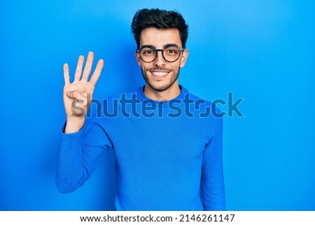 Young hispanic man wearing casual clothes and glasses showing and pointing up with fingers number four while smiling confident and happy. 