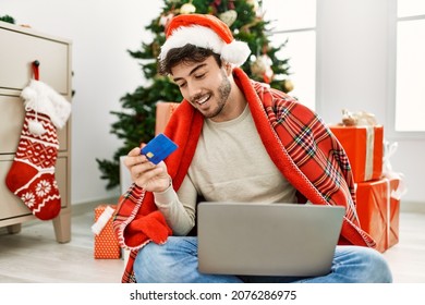 Young Hispanic Man Wearing Christmas Hat Using Laptop And Credit Card At Home.