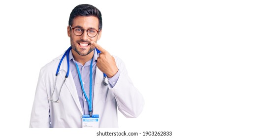 Young Hispanic Man Wearing Doctor Uniform And Stethoscope Pointing With Hand Finger To Face And Nose, Smiling Cheerful. Beauty Concept 