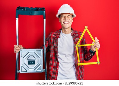Young hispanic man wearing handyman uniform holding construction stairs   house project smiling   laughing hard out loud because funny crazy joke  