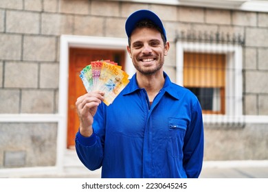 Young hispanic man wearing handyman uniform holding swiss francs looking positive and happy standing and smiling with a confident smile showing teeth  - Shutterstock ID 2230645245
