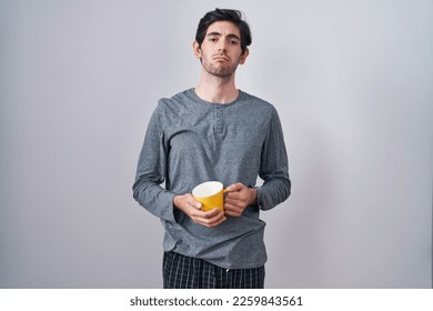 Young hispanic man wearing pajama drinking a cup of coffee depressed and worry for distress, crying angry and afraid. sad expression. 