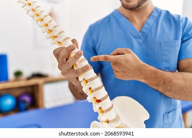 Young hispanic man wearing physio therapist uniform pointing to anatomical model of vertebral column at clinic - Shutterstock ID 2068593941