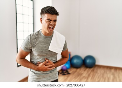 Young Hispanic Man Wearing Sportswear And Towel At The Gym With Hand On Stomach Because Indigestion, Painful Illness Feeling Unwell. Ache Concept. 