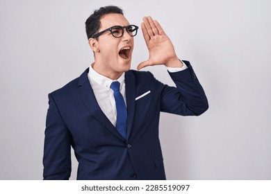 Young hispanic man wearing suit and tie shouting and screaming loud to side with hand on mouth. communication concept. 