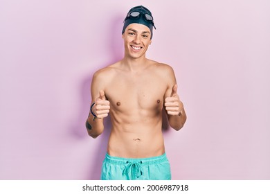 Young hispanic man wearing swimwear and swimmer glasses success sign doing positive gesture with hand, thumbs up smiling and happy. cheerful expression and winner gesture.  - Powered by Shutterstock