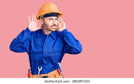 Young Hispanic Man Wearing Worker Uniform Trying To Hear Both Hands On Ear Gesture, Curious For Gossip. Hearing Problem, Deaf 