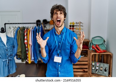 Young hispanic man working as manager at retail boutique crazy and mad shouting and yelling with aggressive expression and arms raised. frustration concept. 