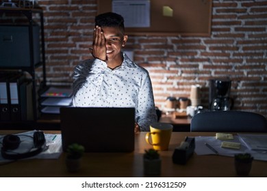 Young hispanic man working at the office at night covering one eye with hand, confident smile on face and surprise emotion.  - Shutterstock ID 2196312509