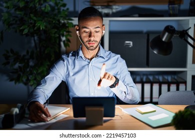 Young Hispanic Man Working At The Office At Night Pointing With Finger Up And Angry Expression, Showing No Gesture 