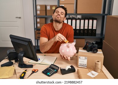 Young Hispanic Man Working At Small Business Ecommerce Holding Piggy Bank Looking At The Camera Blowing A Kiss Being Lovely And Sexy. Love Expression. 