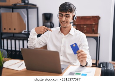 Young hispanic man working using computer laptop holding credit card looking confident with smile on face, pointing oneself with fingers proud and happy. 