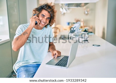 Young hispanic man working using smartphone and laptop at home.