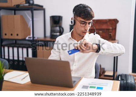 Young hispanic man working using computer laptop holding credit card looking at the watch time worried, afraid of getting late 