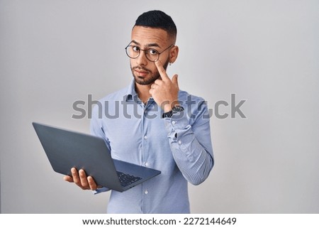 Young hispanic man working using computer laptop pointing to the eye watching you gesture, suspicious expression 