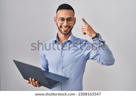 Young hispanic man working using computer laptop smiling amazed and surprised and pointing up with fingers and raised arms. 