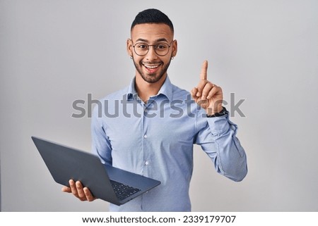 Young hispanic man working using computer laptop pointing finger up with successful idea. exited and happy. number one. 
