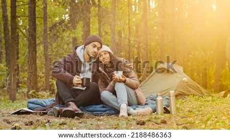 Young hispanic married couple tourists rest in woods camping man and woman in love drinking hot tea talking cute loving guy hugging girl spend nice time together smile communicate travel in nature