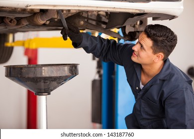 Young Hispanic mechanic draining engine oil from a car for an oil change at an auto shop