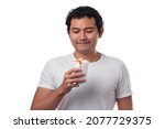 A young Hispanic, Mexican, eats corn in a cup, esquite, with white cheese and hot sauce, dressed in a white shirt with a white background, smiling