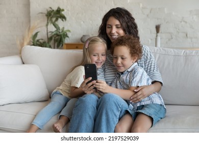 Young Hispanic Mom Her Children Spend Free Time On Internet, Rest On Sofa Holding Modern Smartphone Watch Video Vlog Or Cartoons, Enjoy New Virtual On-line Game Or New Mobile App. Fun, Leisure Concept