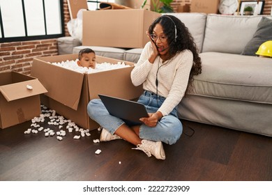 Young Hispanic Mother And Kid Sitting On The Floor At New Home Using Laptop Scared And Amazed With Open Mouth For Surprise, Disbelief Face 