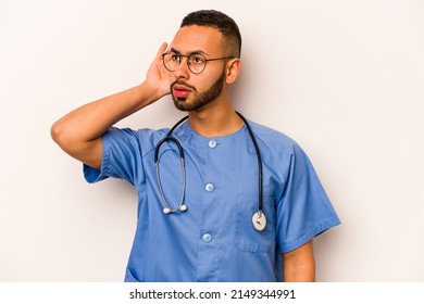 Young Hispanic Nurse Man Isolated On White Background Trying To Listening A Gossip.