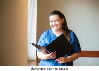 Young Hispanic Nurse Smiling, Holding A Report And Looking Into Camera