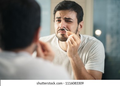 Young Hispanic People And Male Beauty. Metrosexual Man Feeling Pain When Trimming Nose Hair With Tweezers