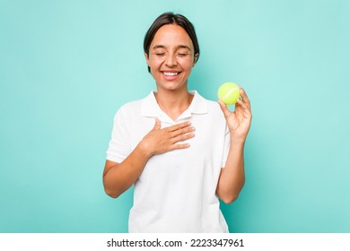 Young Hispanic Physiotherapy Holding A Tennis Ball Isolated On Blue Background Laughs Out Loudly Keeping Hand On Chest.