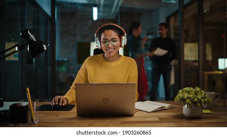 Young Hispanic Project Manager in Headphones and Working on Laptop Computer in Busy Creative Office Environment. Beautiful Diverse Multiethnic Female Specialist is Writing Business Strategy. - Powered by Shutterstock