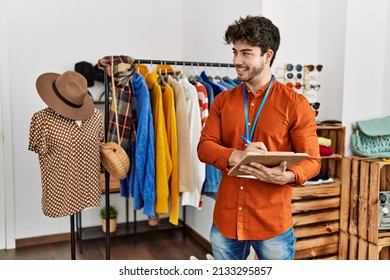 Young Hispanic Shopkeeper Man Smiling Happy Writing On Clipboard Working At Clothing Store.