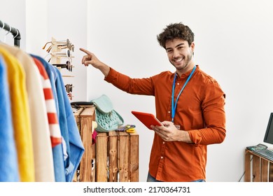 Young Hispanic Shopkeeper Man Smiling Happy Using Touchpad Working At Clothing Store.