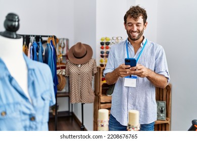 Young hispanic shopkeeper man using smartphone working at clothing store. - Powered by Shutterstock