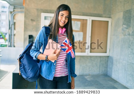 Young hispanic student girl smiling happy holding book and uk flag at the university.