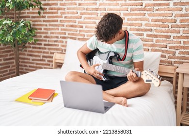 Adolescente hispánica joven con clase de guitarra eléctrica en línea sentada en la cama en el dormitorio