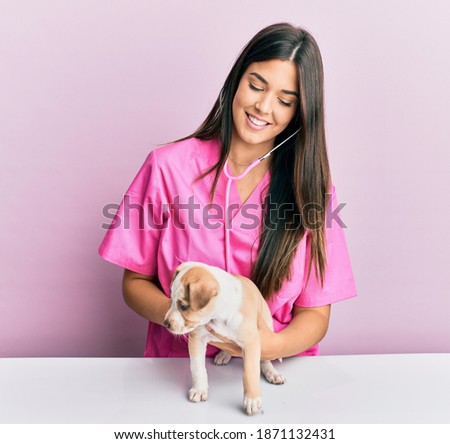 Young hispanic veterinarian girl smiling happy examining little dog at the clinic.