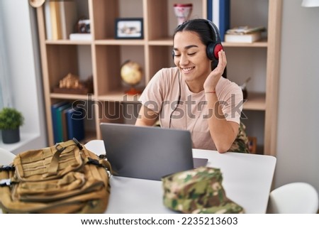 Young hispanic woman army soldier using laptop and headphones at home