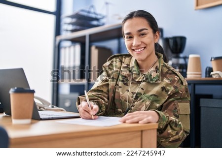 Young hispanic woman army soldier using laptop writing on document at office