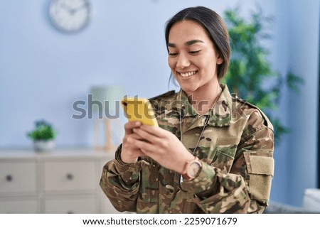 Young hispanic woman army soldier using smartphone at home