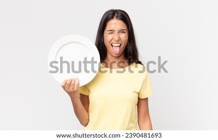 young hispanic woman with cheerful and rebellious attitude, joking and sticking tongue out and holding an empty plate