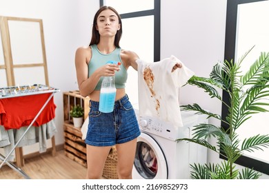 Young Hispanic Woman Cleaning Dirty White T Shirt With Stain At Laundry Room Puffing Cheeks With Funny Face. Mouth Inflated With Air, Catching Air. 