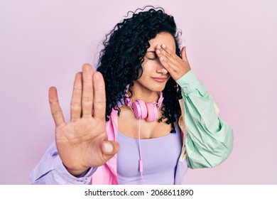 Young hispanic woman with curly hair wearing gym clothes and using headphones covering eyes with hands and doing stop gesture with sad and fear expression. embarrassed and negative concept.  - Powered by Shutterstock