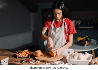 Young Hispanic Woman Cutting Sweet Potato While Cooking In Kitchen At Home