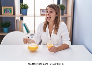 Young Hispanic Woman Drinking Glass Of Orange Juice Celebrating Crazy And Amazed For Success With Open Eyes Screaming Excited. 